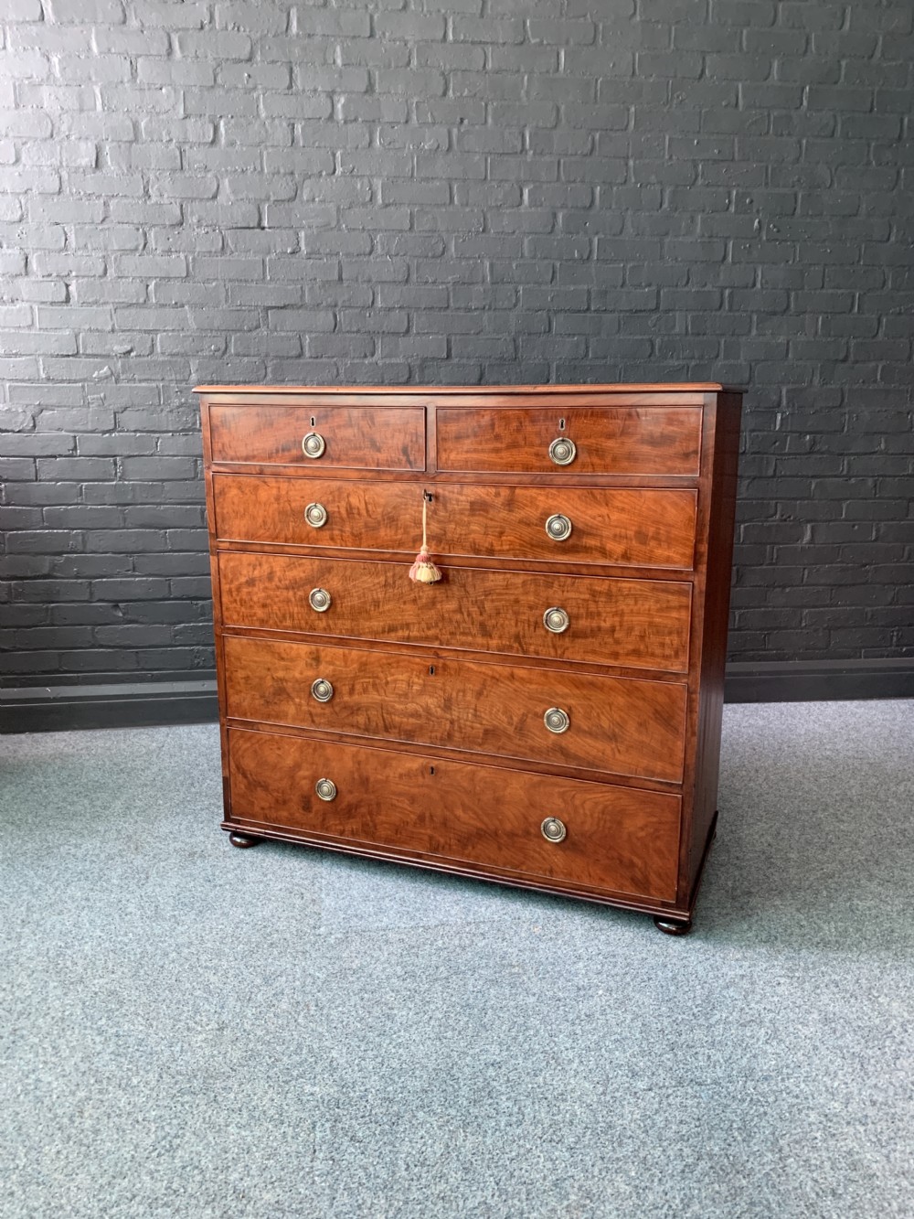 A 19th-century flame mahogany chest of drawers featuring two short drawers above four long drawers with brass circular handles, set on turned feet.