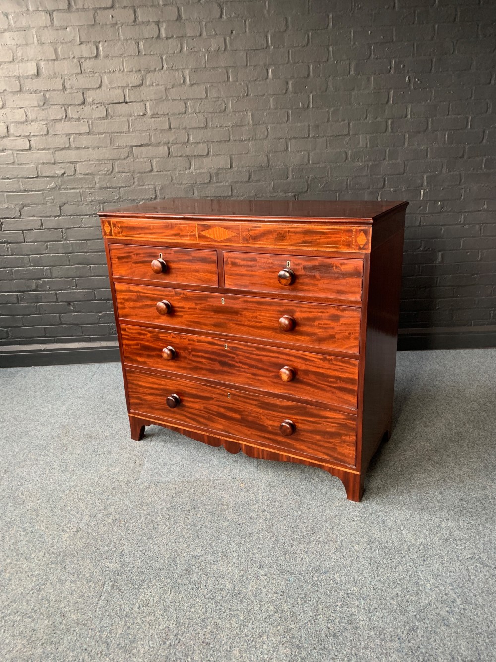 A 19th-century inlaid mahogany chest of drawers featuring two short over three long drawers with turned wooden knobs and bracket feet.