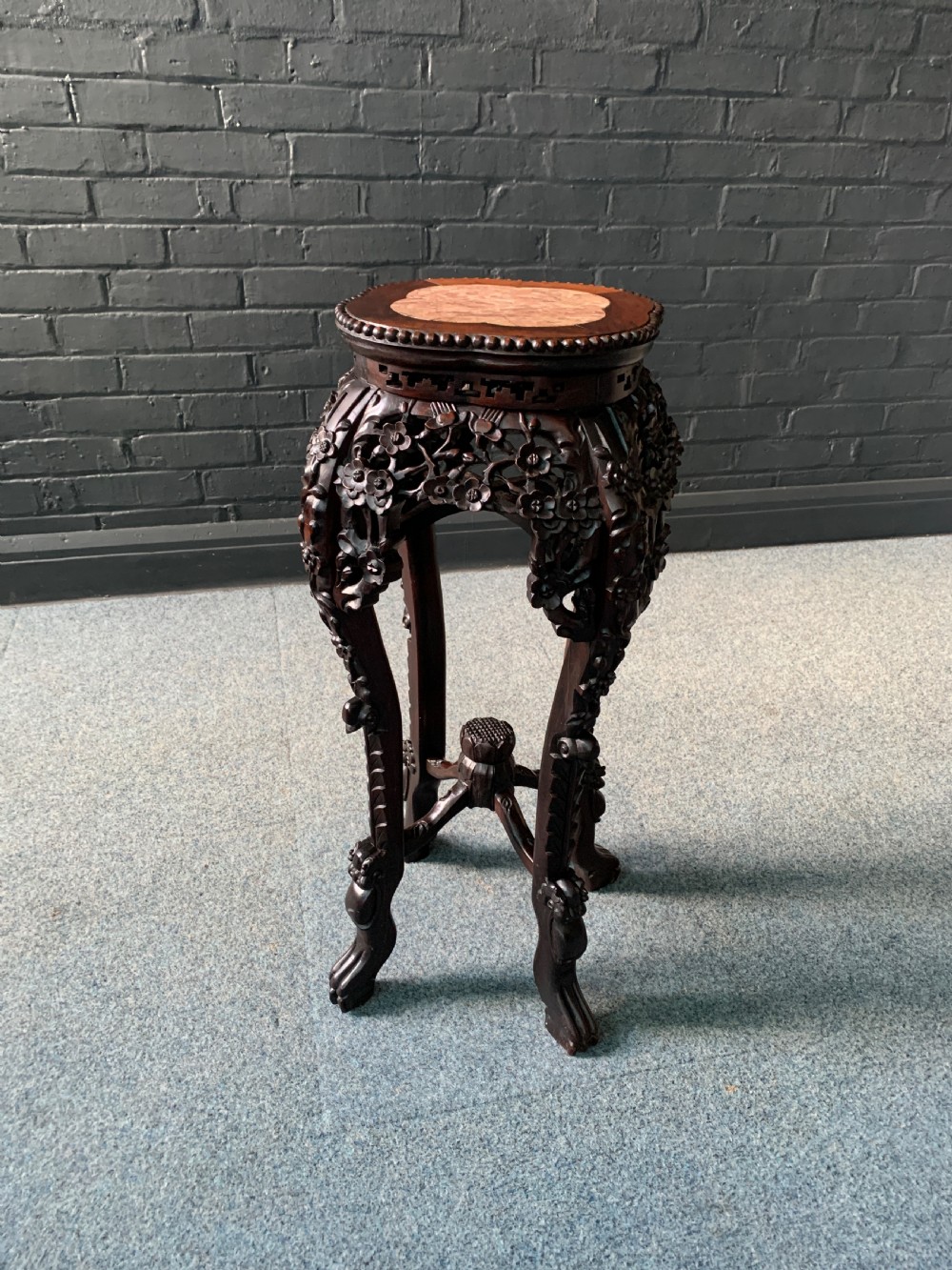 A 19th-century Chinese dark hardwood plant stand featuring an inset pink marble top, relief floral carvings, cabriole legs, and an X-form stretcher.