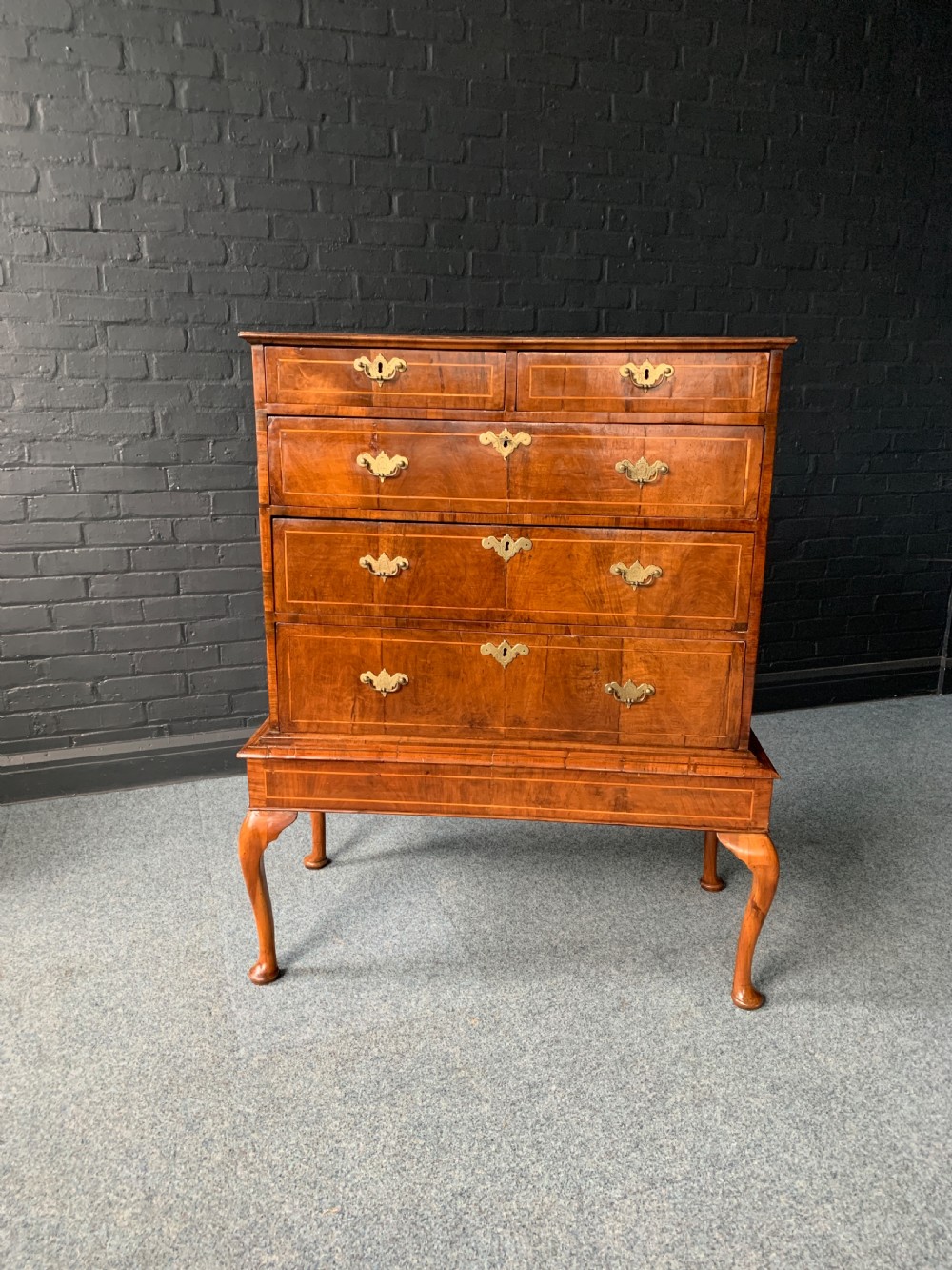A George II walnut chest on stand featuring crossbanded drawer fronts, brass plate handles, and cabriole legs on pad feet.