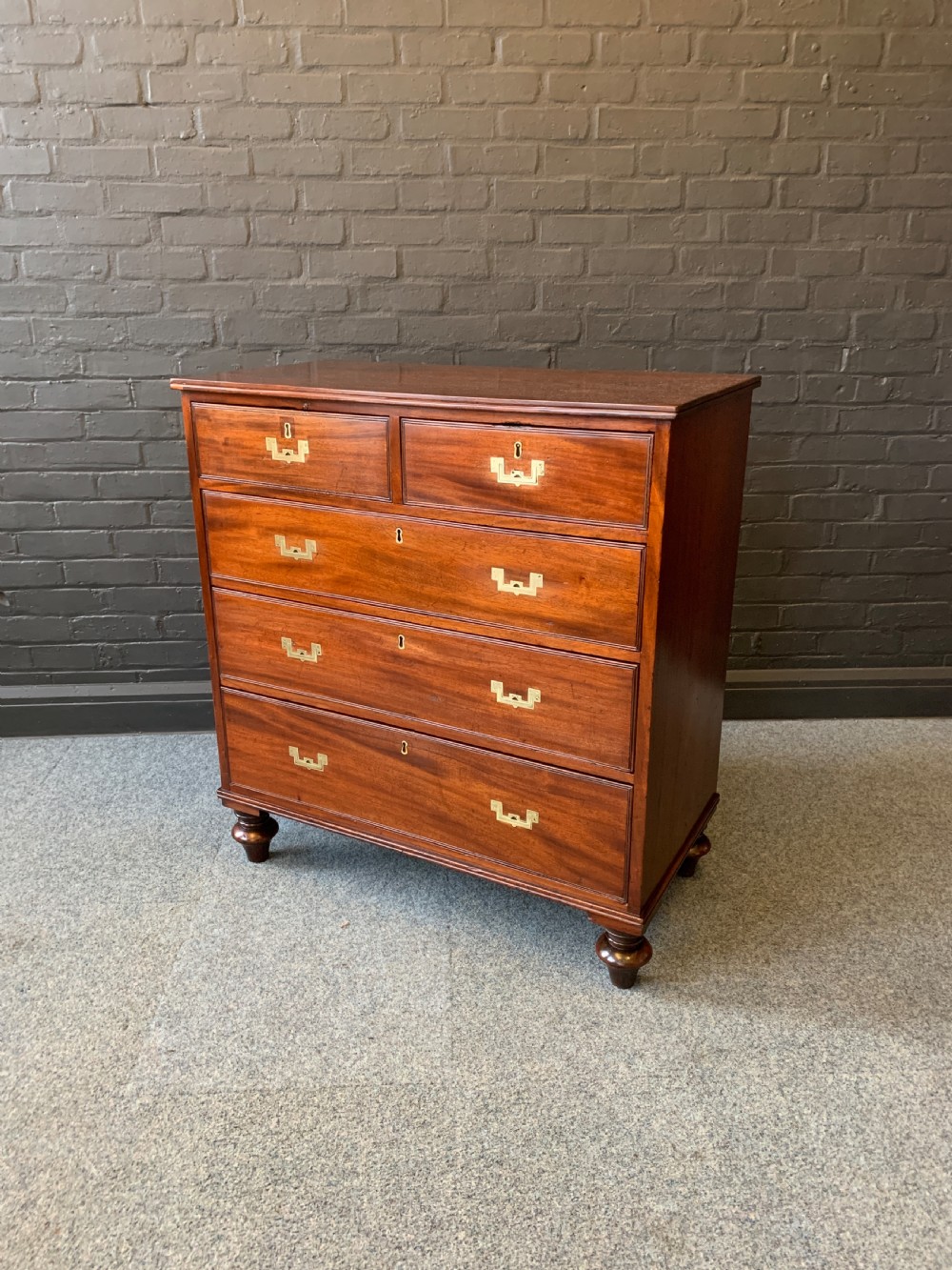 A nineteenth-century mahogany military campaign chest featuring a two-over-three drawer configuration with flush brass handles and keyholes, raised on turned feet.