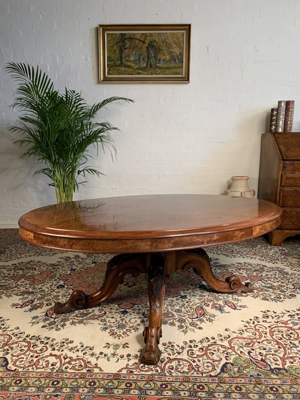 A Victorian oval low coffee table made from polished burr walnut featuring an intricately carved quadruped scroll pedestal base.