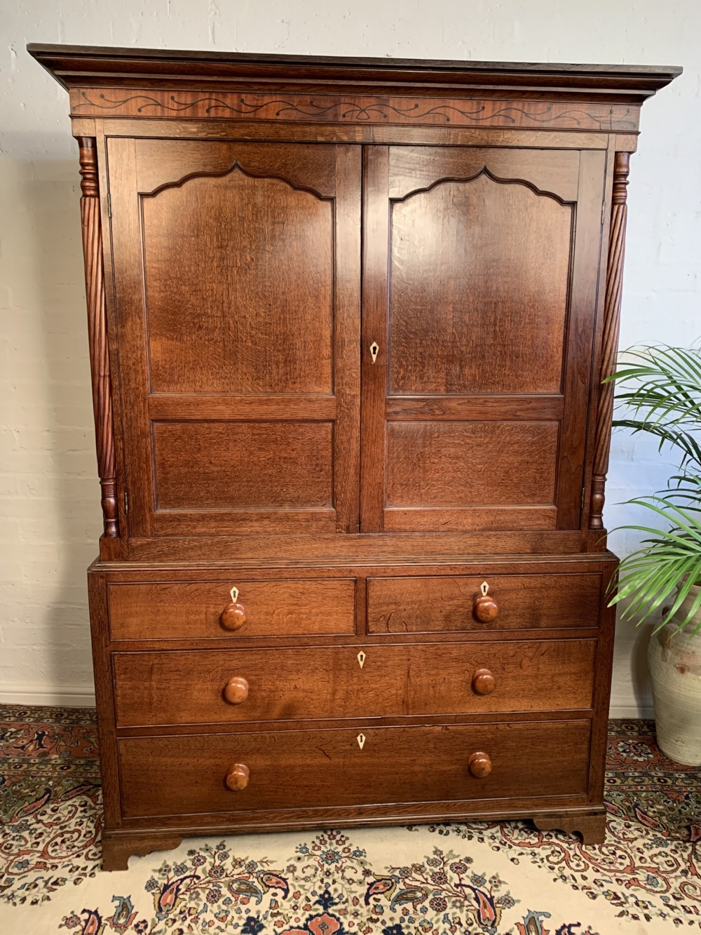 A nineteenth-century two-stage Welsh oak press cupboard featuring arched panel doors, barley twist side columns, an inlaid frieze, and a lower chest of drawers.