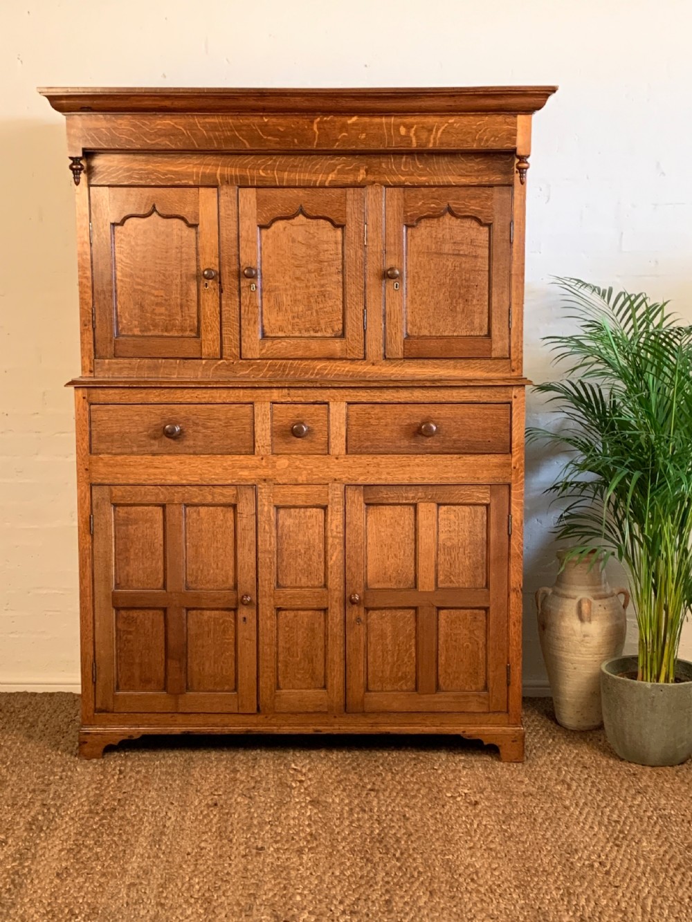 A 19th-century two-tier Welsh oak deuddarn cupboard featuring ogee arched panel doors, turned wooden knobs, and a moulded cornice.