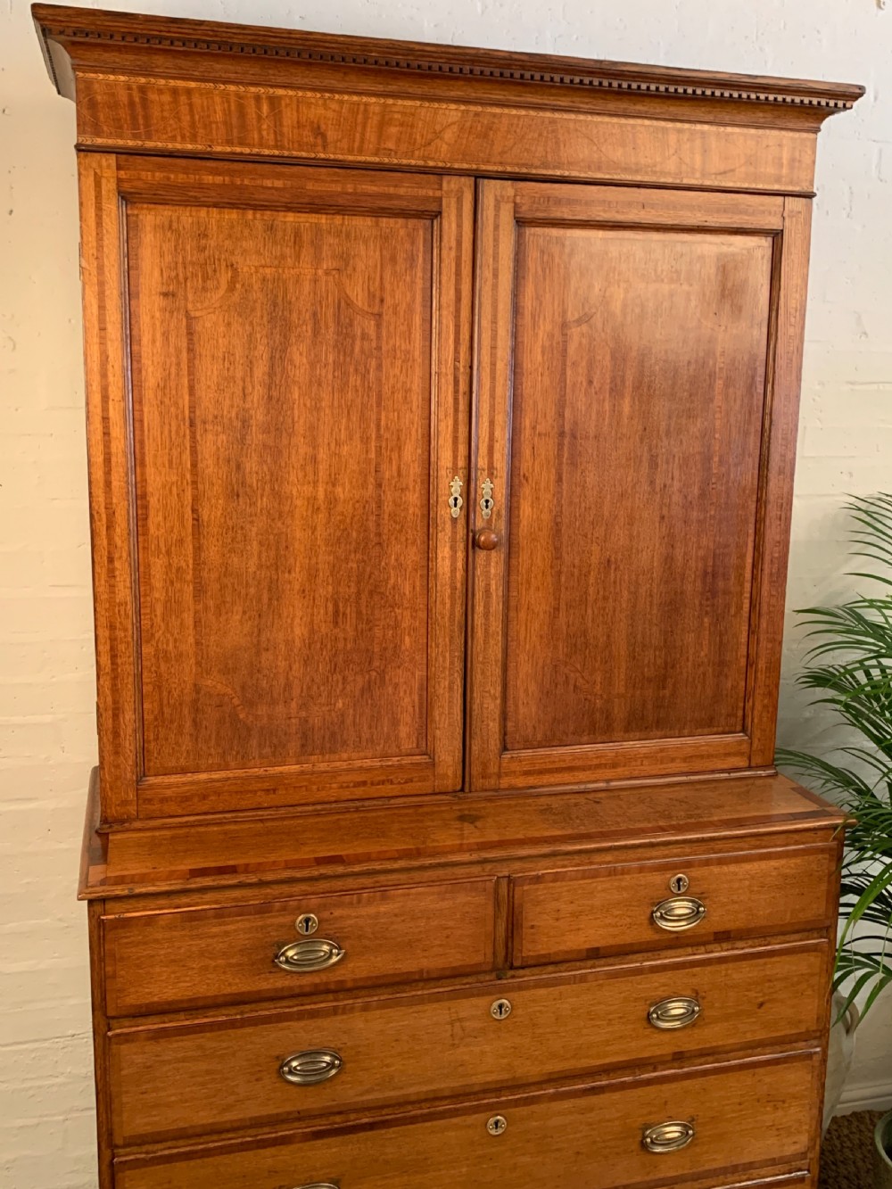 A two-stage Georgian oak press cupboard featuring a double-door upper cabinet mounted over a chest of drawers with oval brass handles. View II