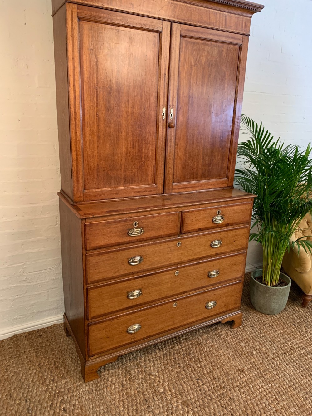 A two-stage Georgian oak press cupboard featuring a double-door upper cabinet mounted over a chest of drawers with oval brass handles. View V
