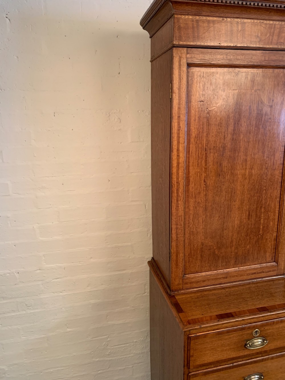 A two-stage Georgian oak press cupboard featuring a double-door upper cabinet mounted over a chest of drawers with oval brass handles. View VI