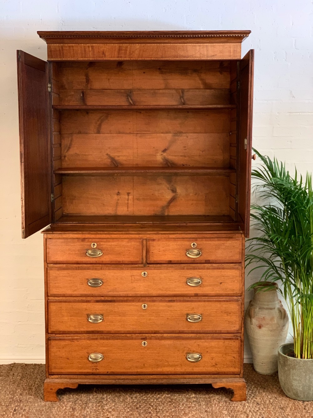 A two-stage Georgian oak press cupboard featuring a double-door upper cabinet mounted over a chest of drawers with oval brass handles. View VII