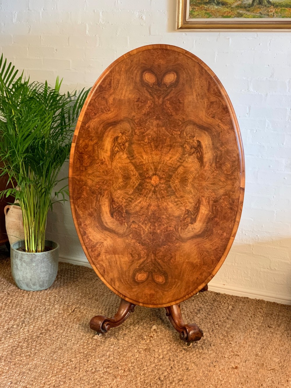 An antique Victorian oval tilt-top centre table made of highly figured burr walnut veneer with a carved pedestal base on castors.