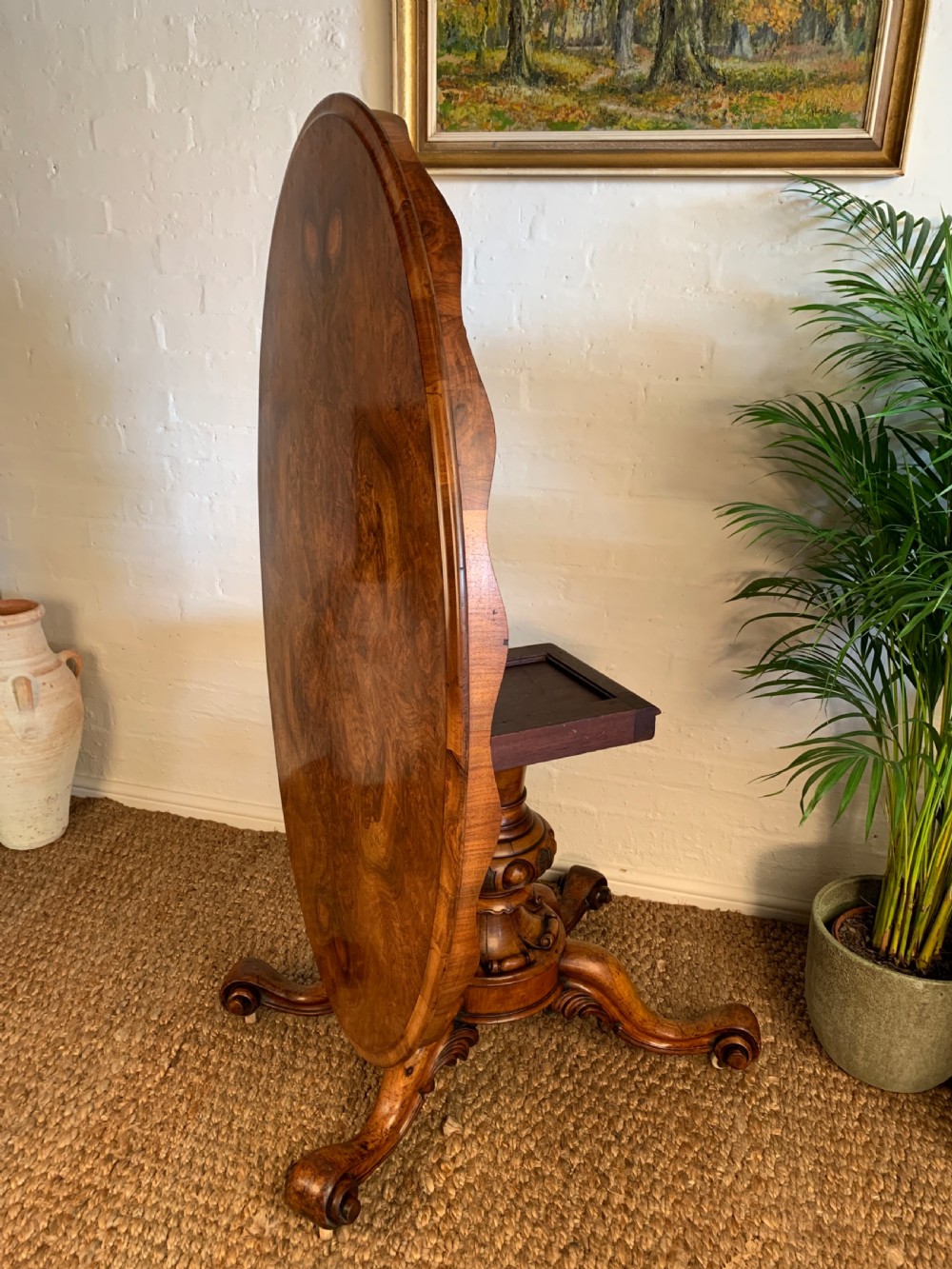An antique Victorian oval tilt-top centre table made of highly figured burr walnut veneer with a carved pedestal base on castors. View III