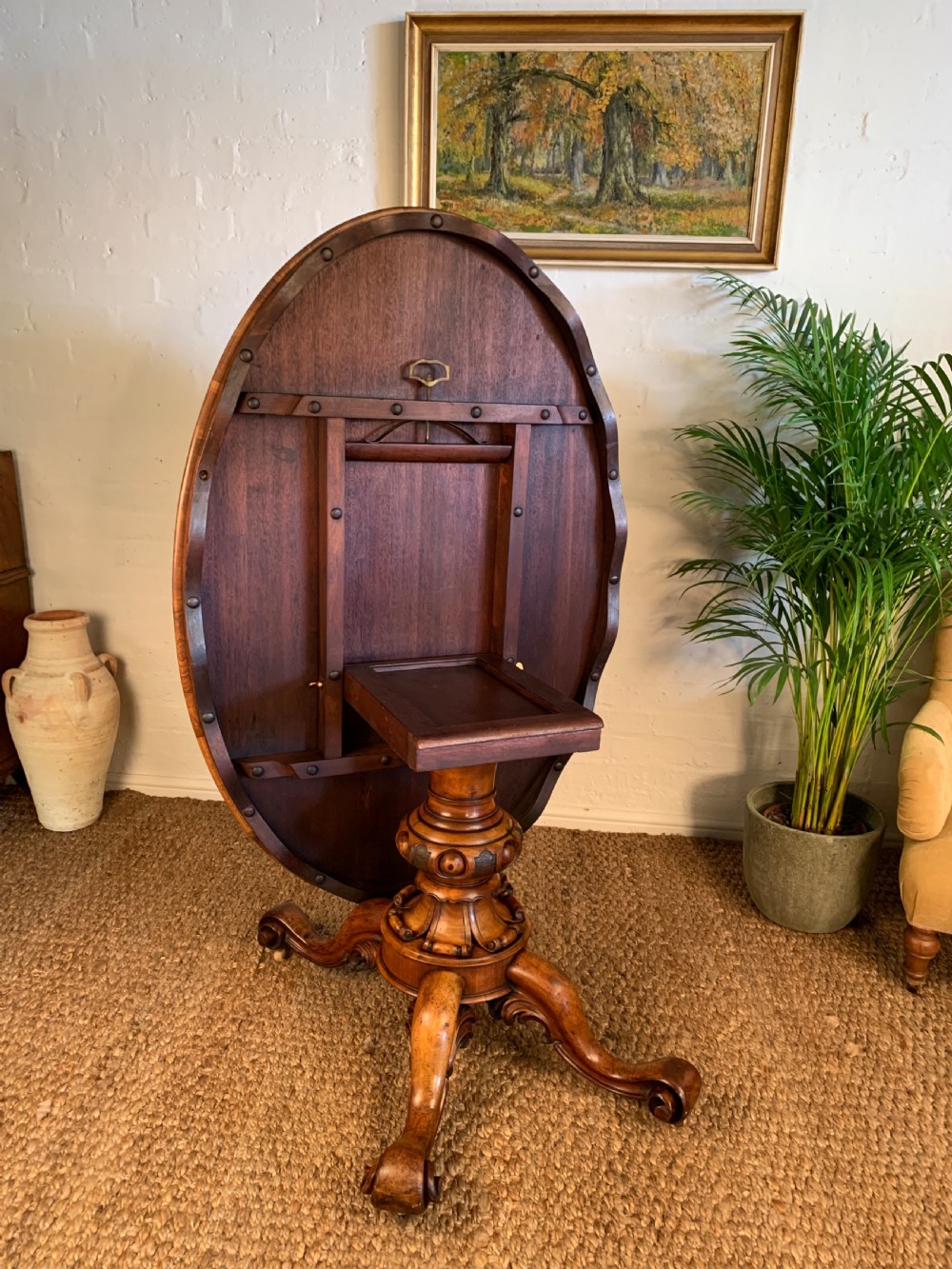 An antique Victorian oval tilt-top centre table made of highly figured burr walnut veneer with a carved pedestal base on castors. View V