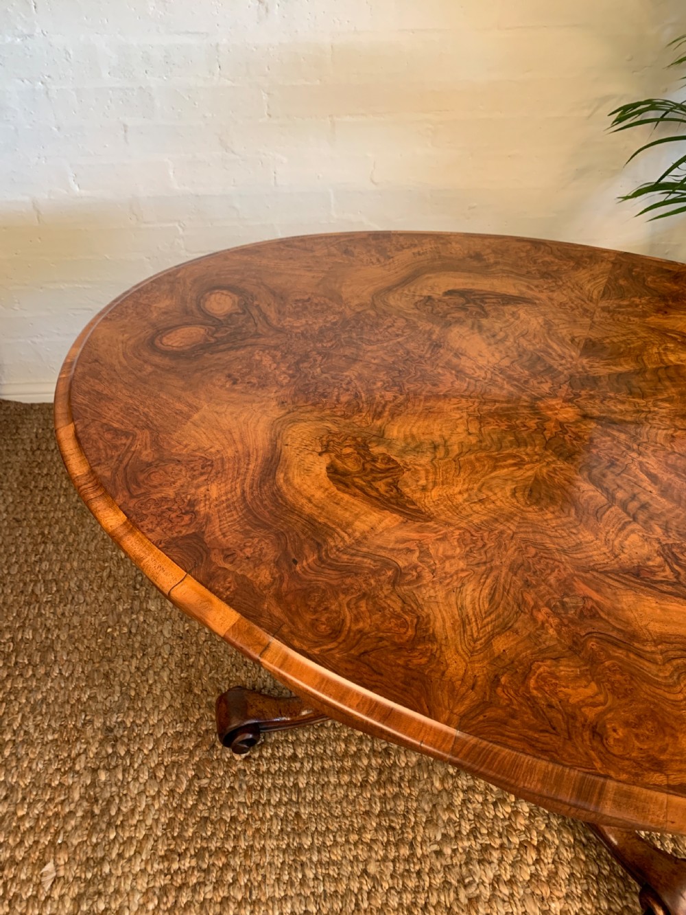 An antique Victorian oval tilt-top centre table made of highly figured burr walnut veneer with a carved pedestal base on castors. View VII