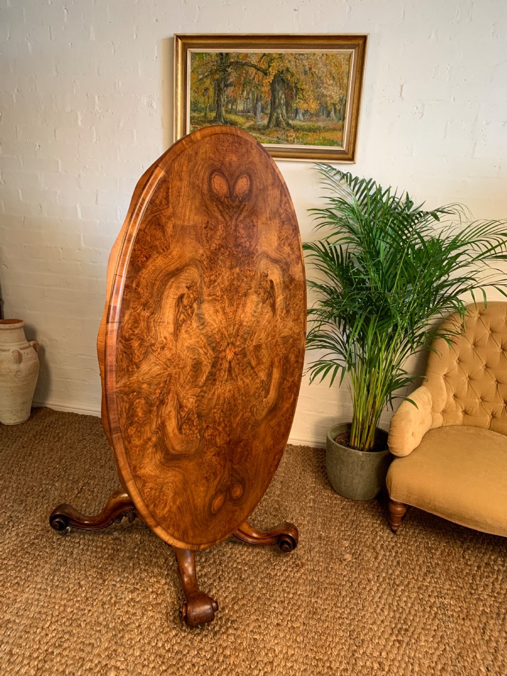 An antique Victorian oval tilt-top centre table made of highly figured burr walnut veneer with a carved pedestal base on castors. View VIII