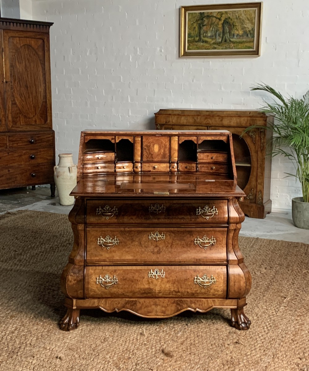 A 19th-century Dutch burr walnut bombe bureau featuring an open slant-front writing surface revealing internal drawers and pigeonholes above three wide serpentine drawers.