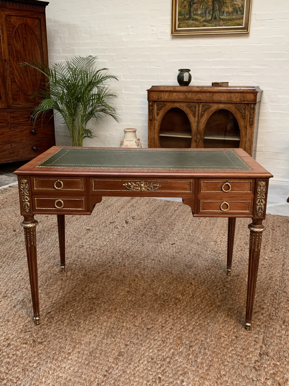 A French mahogany writing desk from circa 1900 featuring a green leather inset top, fluted legs with brass mounts, and drawers with brass ring pulls.
