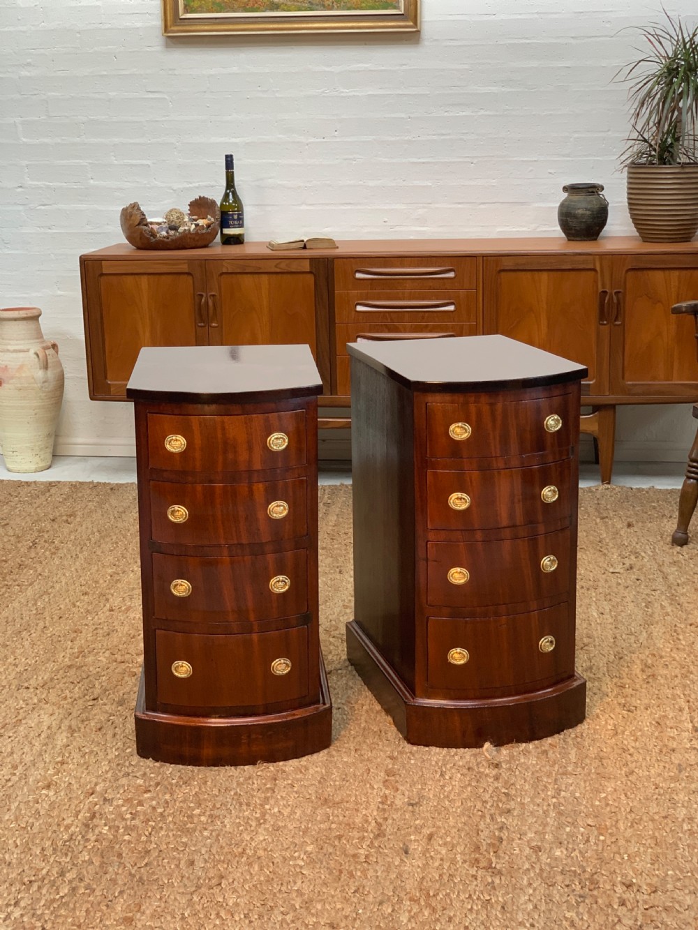 A pair of 19th-century mahogany bedside cabinets featuring curved fronts, four drawers each, brass oval drop handles, and a plinth base.