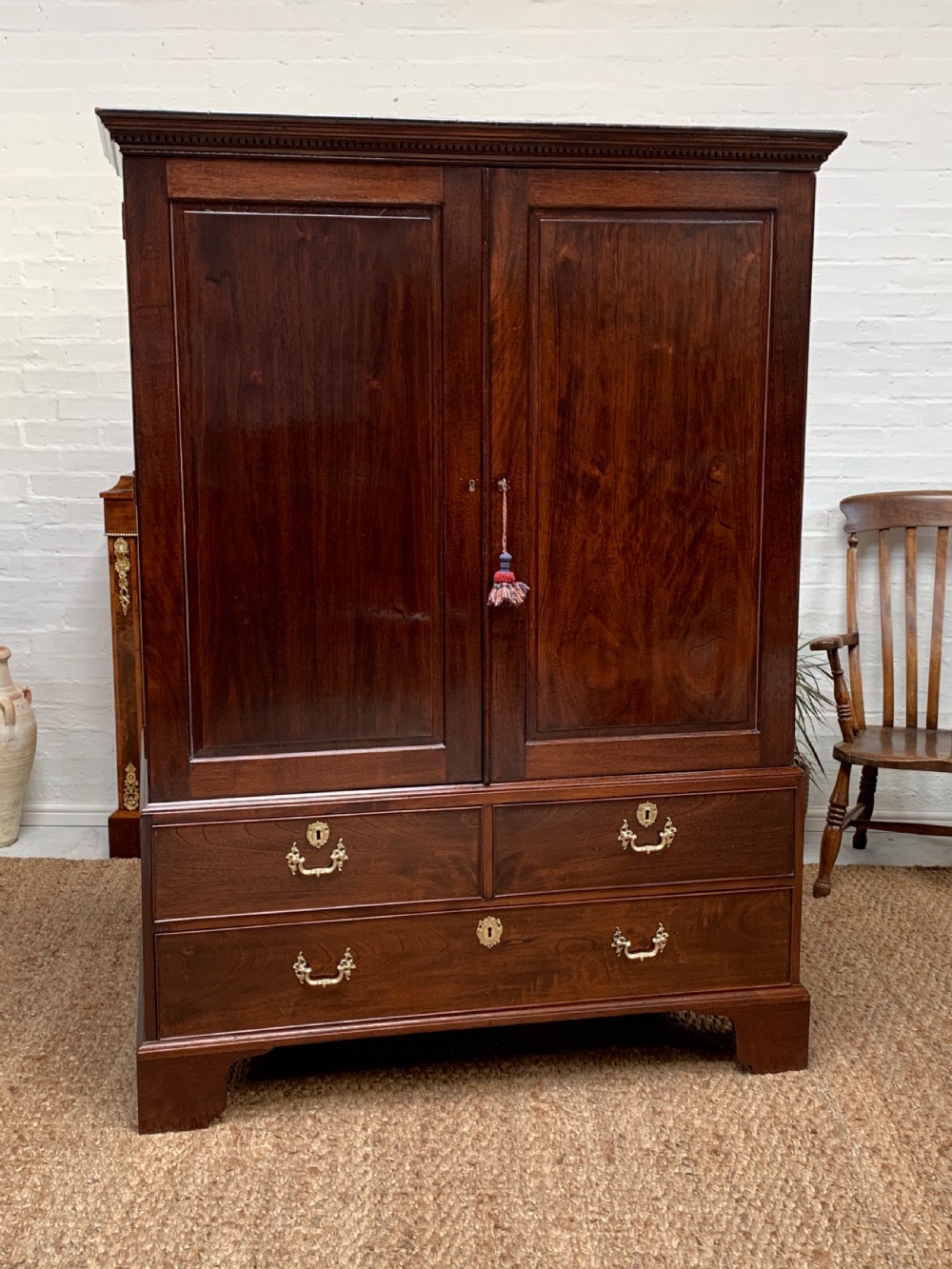 A Georgian dark mahogany linen press featuring two large flame mahogany panelled doors with rosewood crossbanding above two wide drawers with oval brass handles. View II