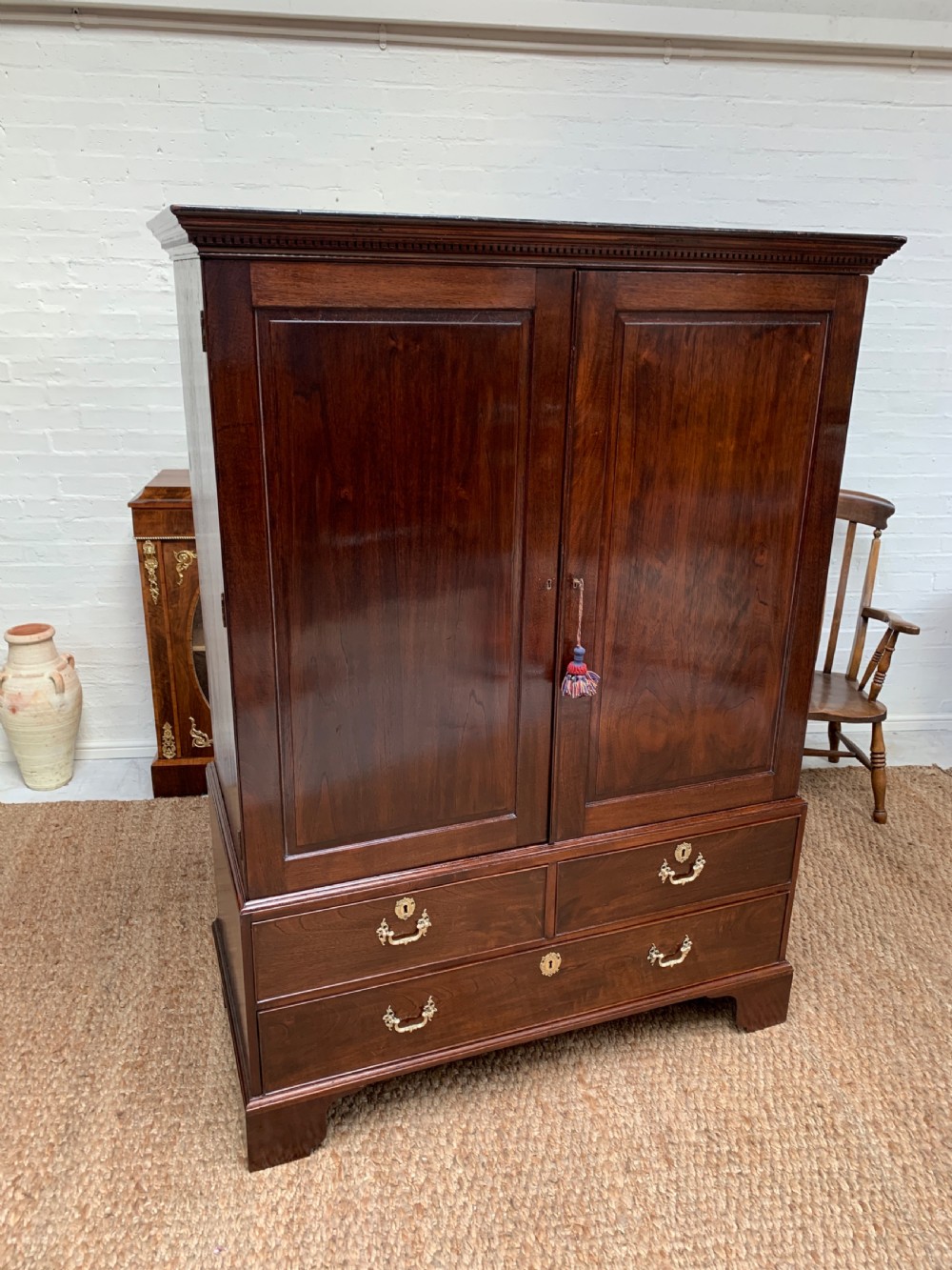 A Georgian dark mahogany linen press featuring two large flame mahogany panelled doors with rosewood crossbanding above two wide drawers with oval brass handles. View V
