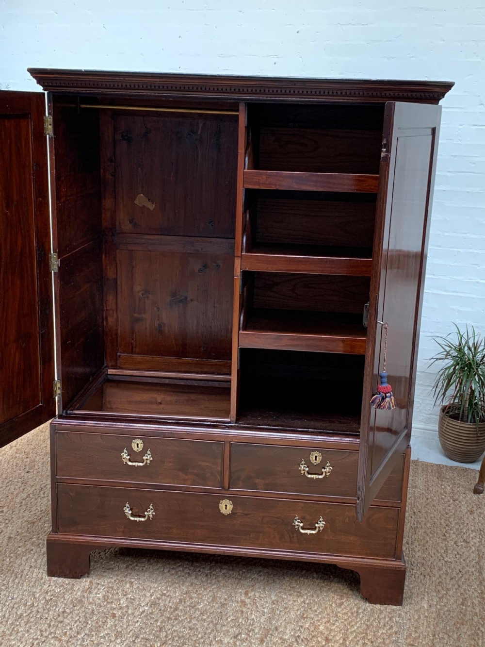 A Georgian dark mahogany linen press featuring two large flame mahogany panelled doors with rosewood crossbanding above two wide drawers with oval brass handles. View VI