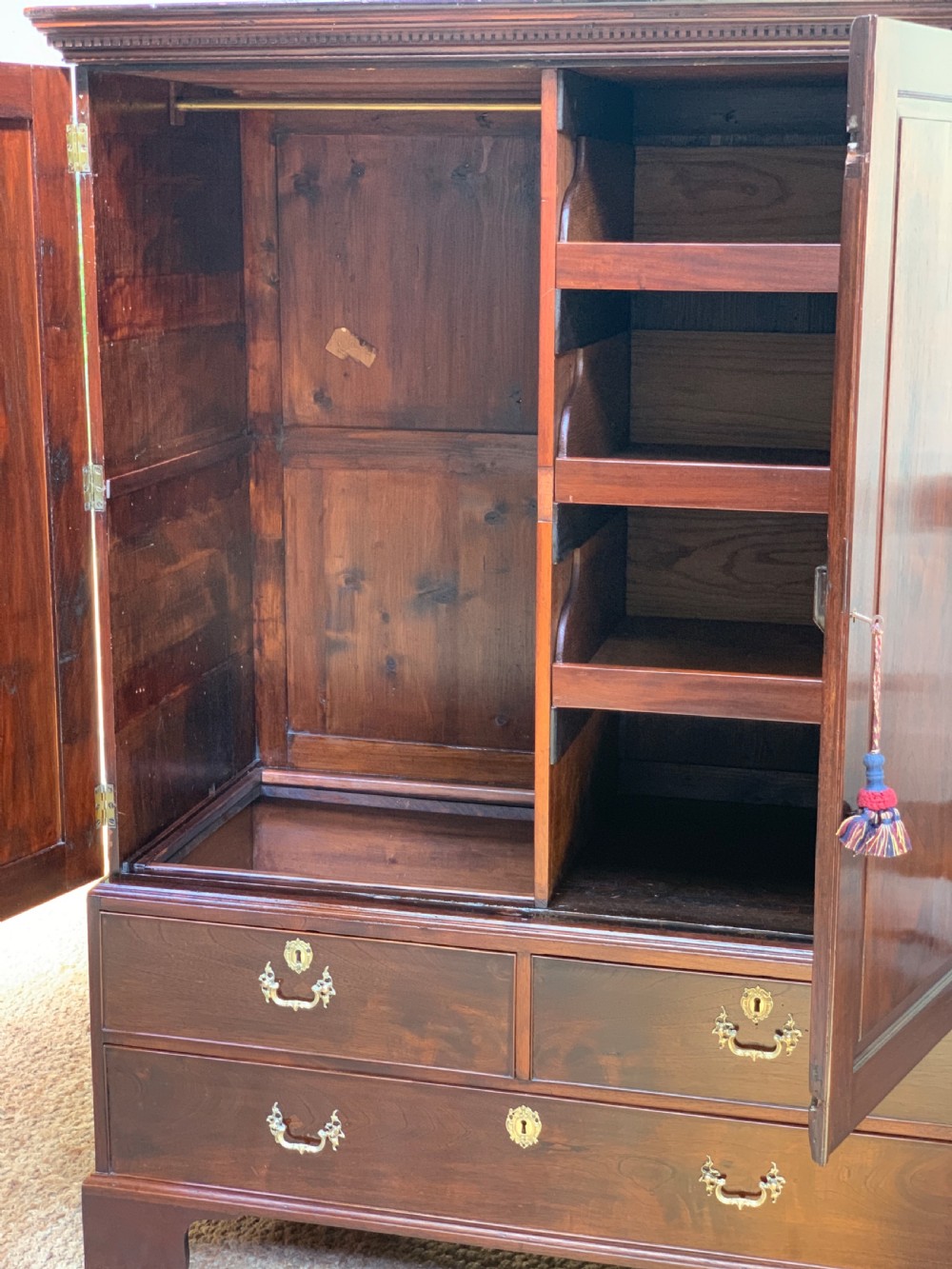 A Georgian dark mahogany linen press featuring two large flame mahogany panelled doors with rosewood crossbanding above two wide drawers with oval brass handles. View VII