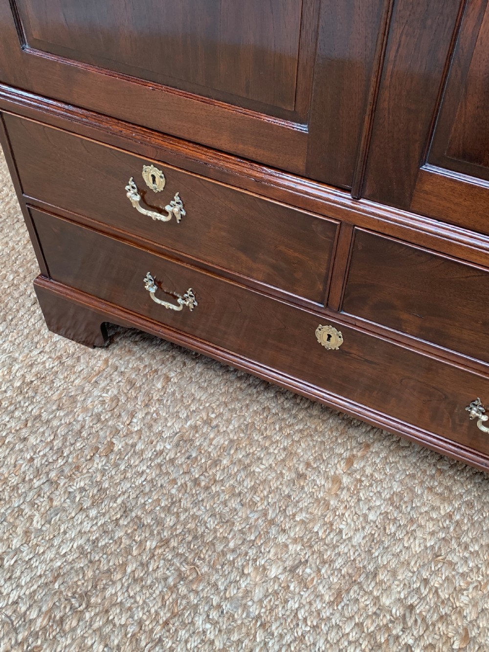 A Georgian dark mahogany linen press featuring two large flame mahogany panelled doors with rosewood crossbanding above two wide drawers with oval brass handles. View X