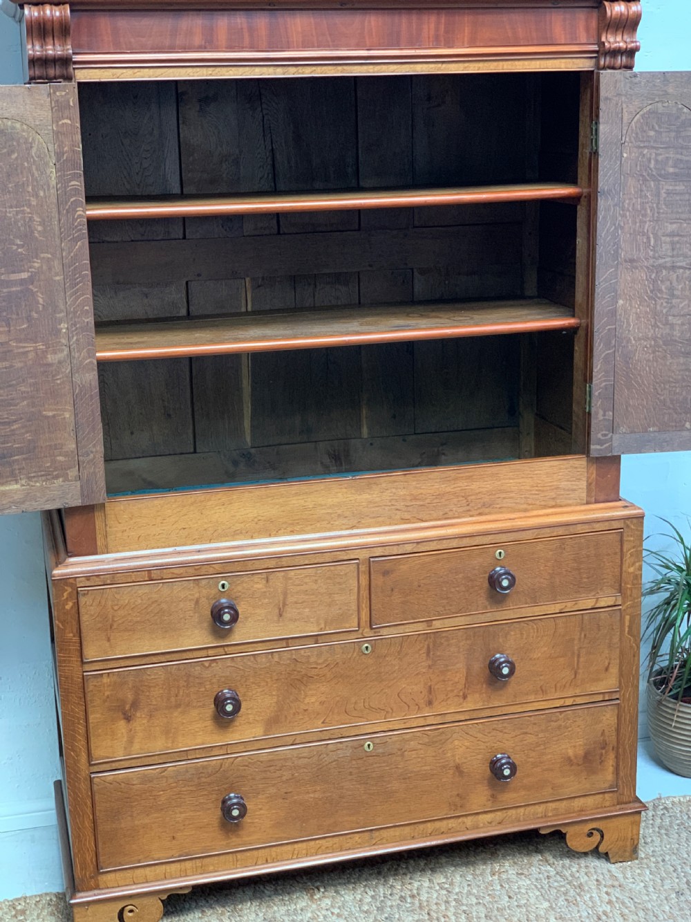 An antique warm brown oak linen press featuring an upper double-door cupboard with arched panels and barley twist columns set over a base with four drawers. View II