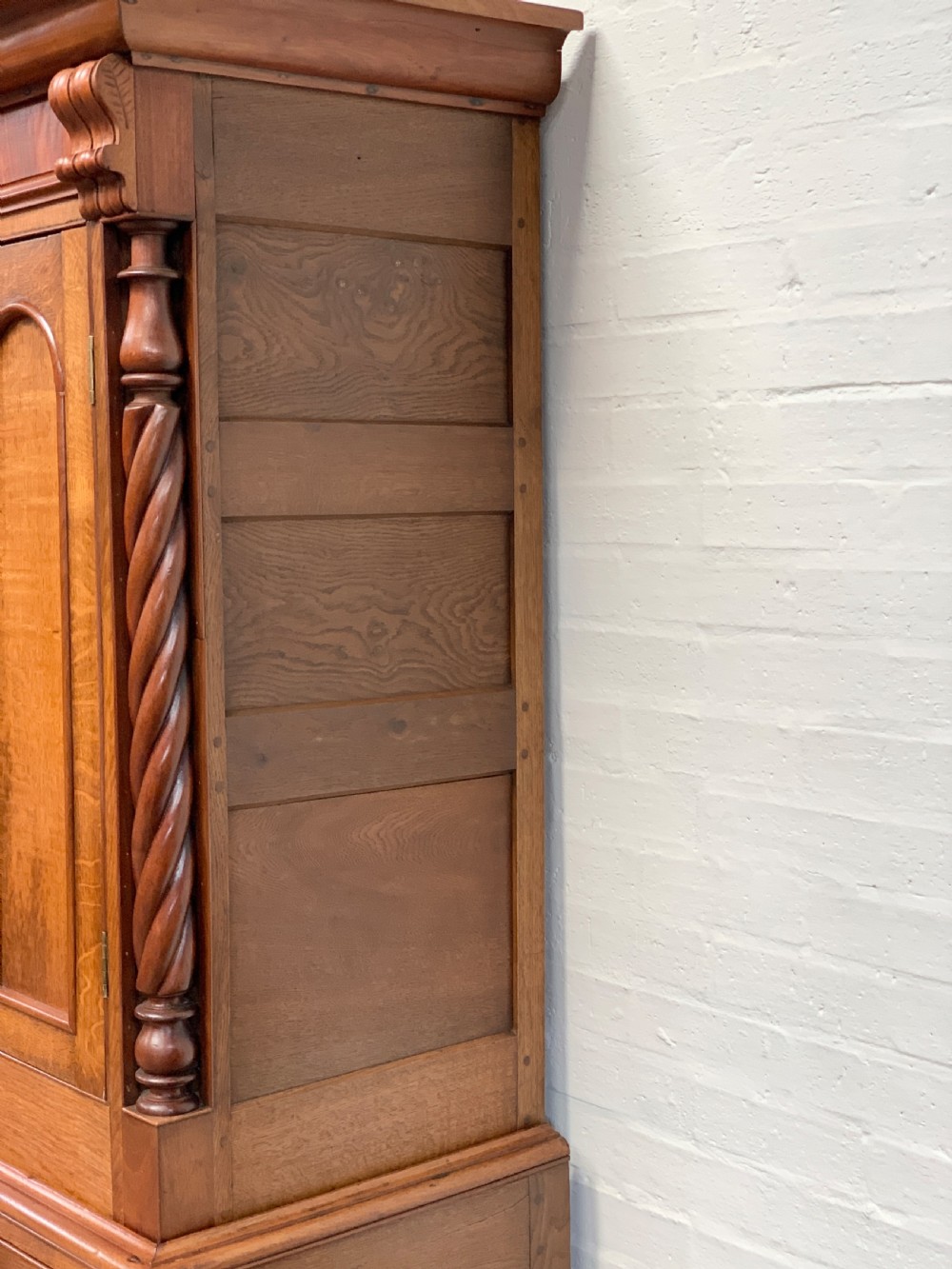 An antique warm brown oak linen press featuring an upper double-door cupboard with arched panels and barley twist columns set over a base with four drawers. View III