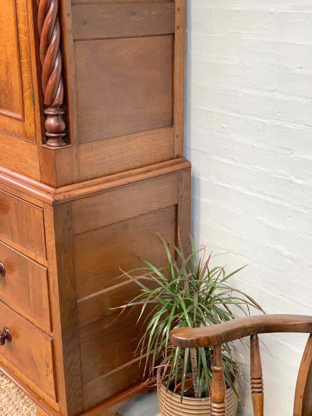 An antique warm brown oak linen press featuring an upper double-door cupboard with arched panels and barley twist columns set over a base with four drawers. View V