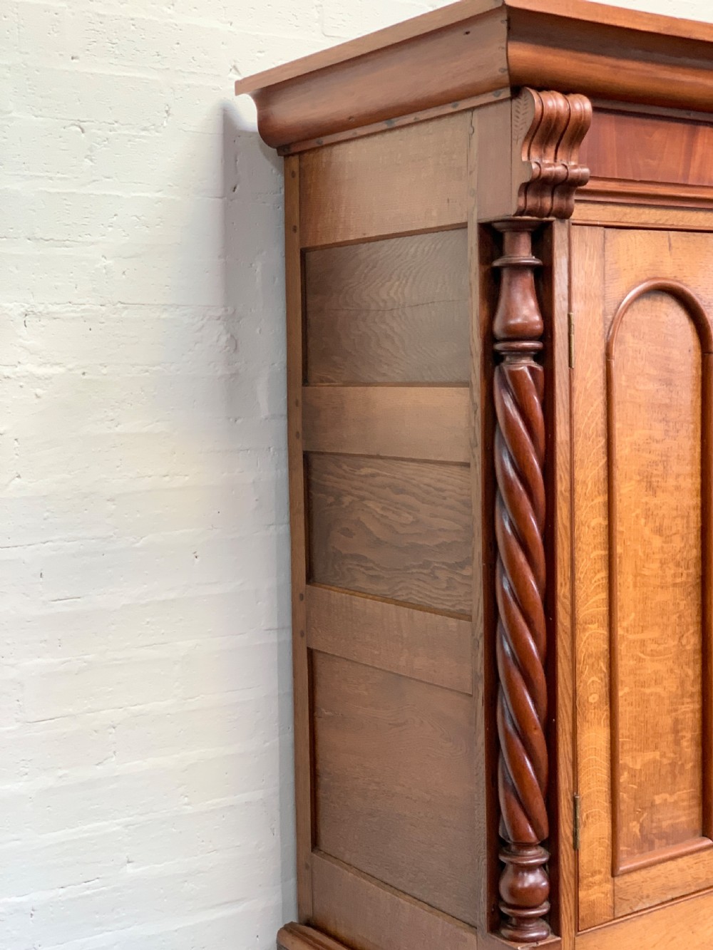 An antique warm brown oak linen press featuring an upper double-door cupboard with arched panels and barley twist columns set over a base with four drawers. View VII