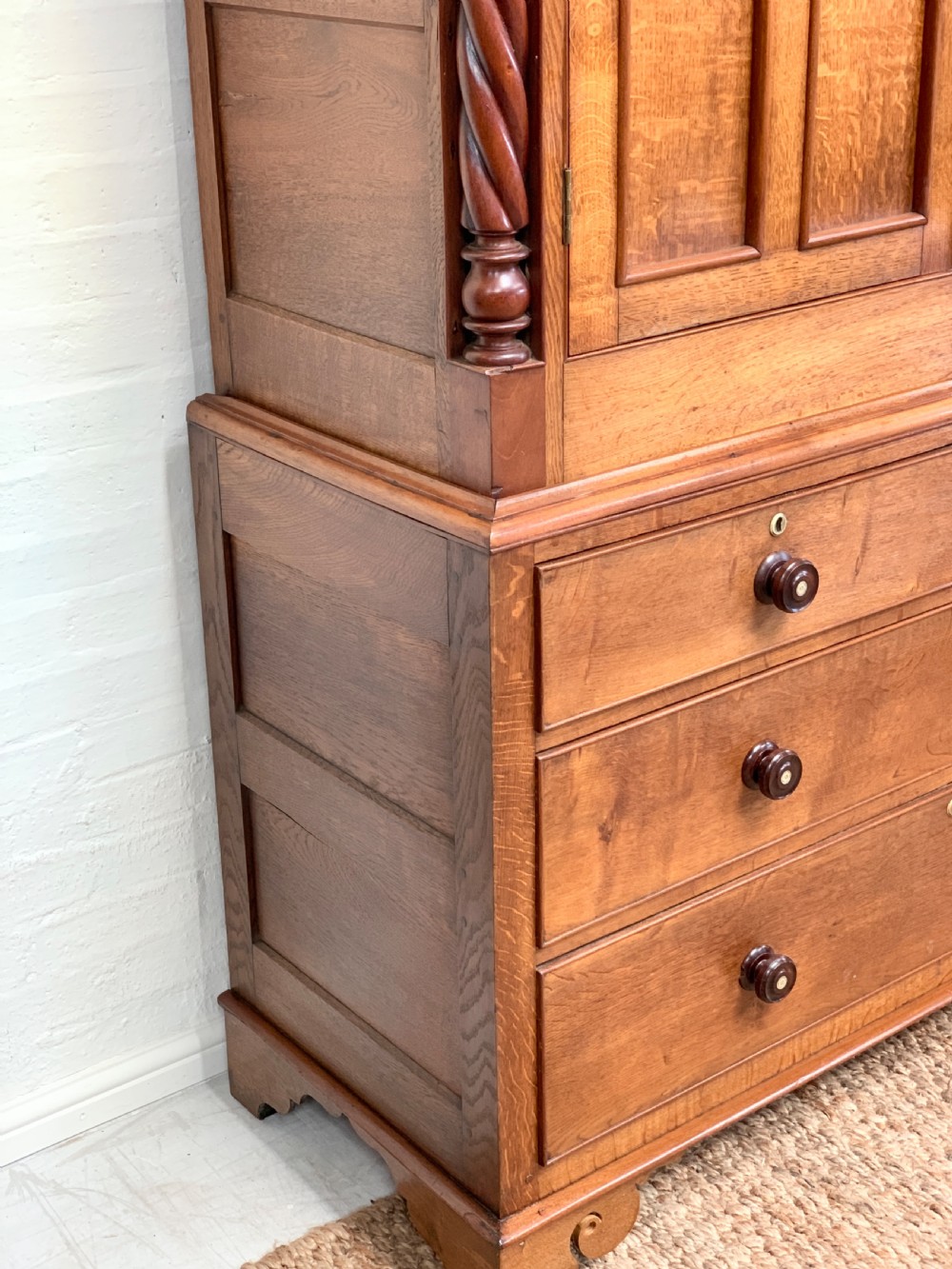 An antique warm brown oak linen press featuring an upper double-door cupboard with arched panels and barley twist columns set over a base with four drawers. View VIII
