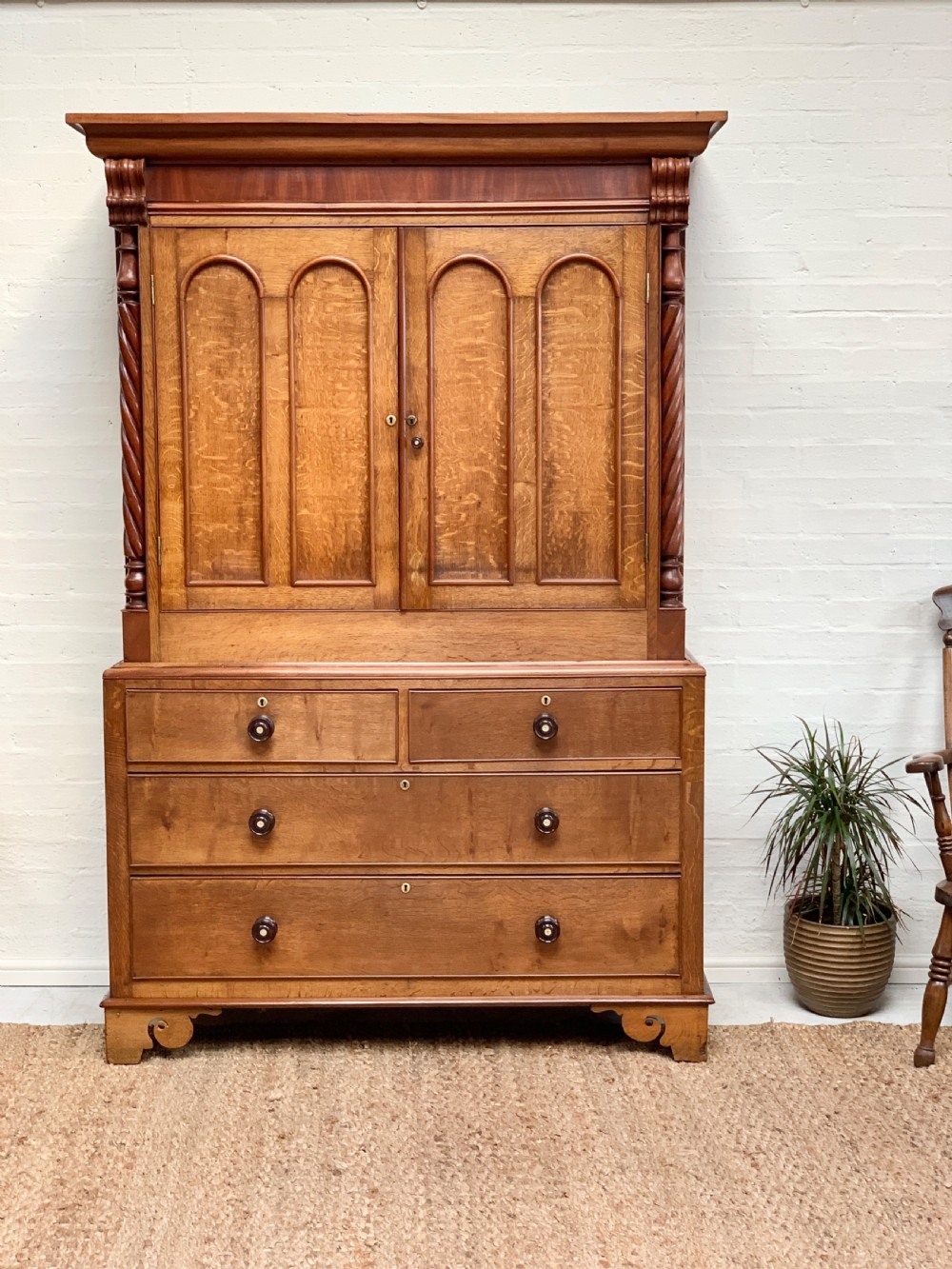 An antique warm brown oak linen press featuring an upper double-door cupboard with arched panels and barley twist columns set over a base with four drawers. View IX