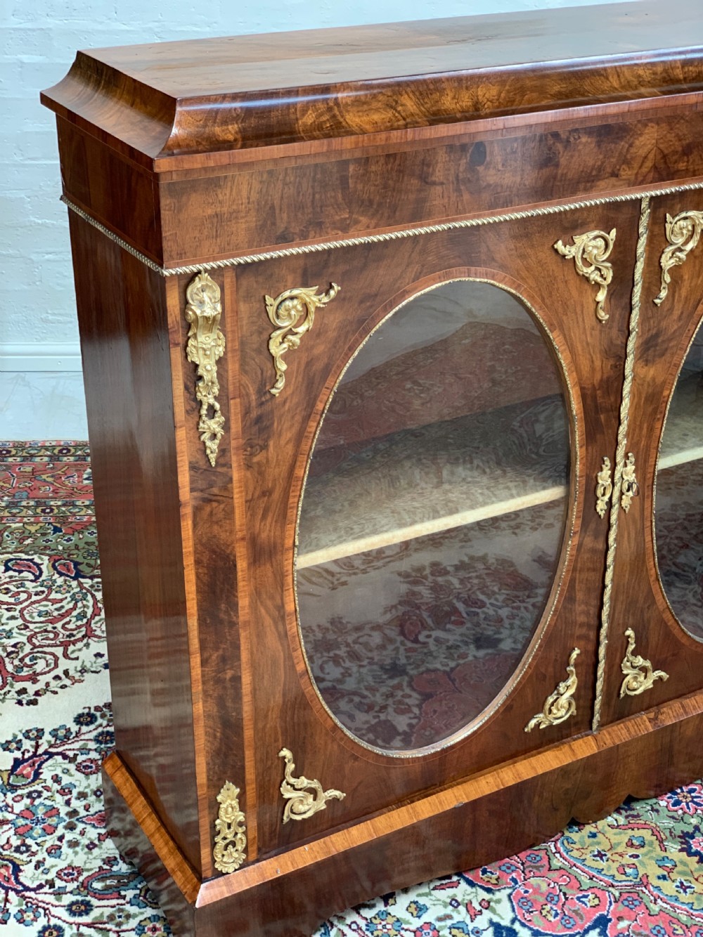 A Victorian double-door pier cabinet featuring figured walnut veneers, oval glass door panels, and decorative brass mounts. View VII