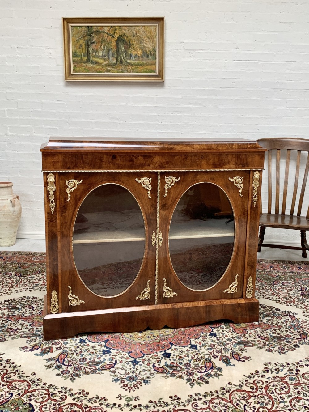 A Victorian double-door pier cabinet featuring figured walnut veneers, oval glass door panels, and decorative brass mounts.