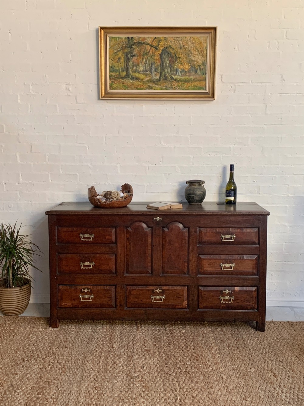 A dark oak mule chest featuring a hinged top, raised arched panels, multiple lower drawers, and brass batwing handles.