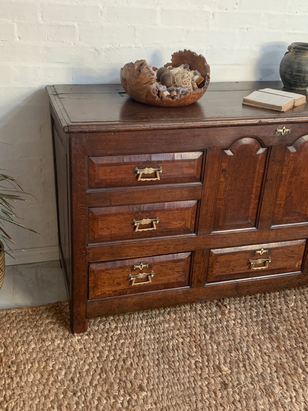 A dark oak mule chest featuring a hinged top, raised arched panels, multiple lower drawers, and brass batwing handles. View II