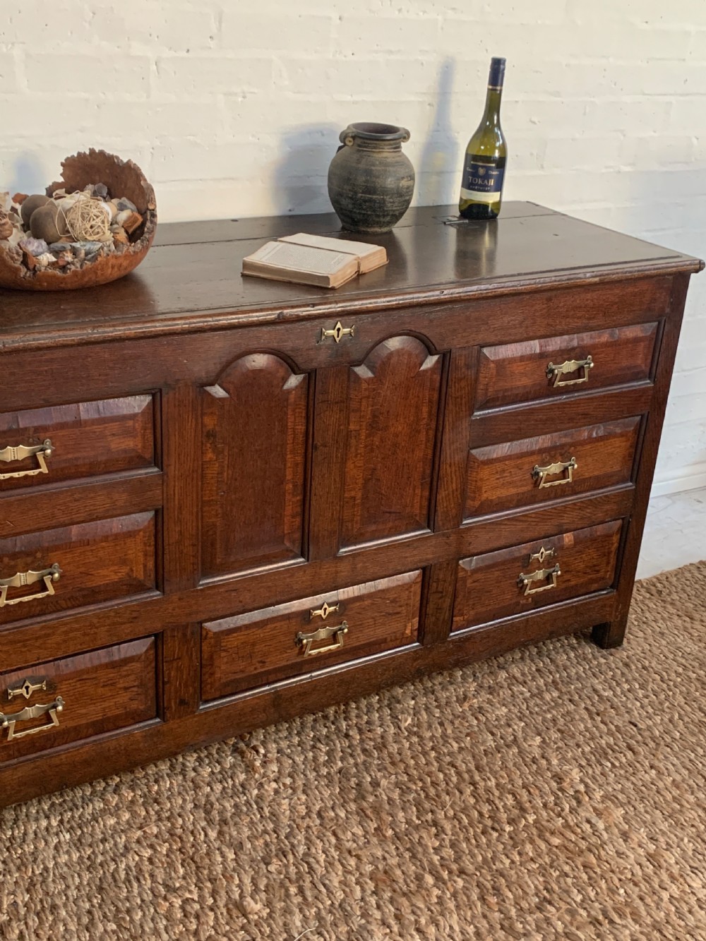 A dark oak mule chest featuring a hinged top, raised arched panels, multiple lower drawers, and brass batwing handles. View III