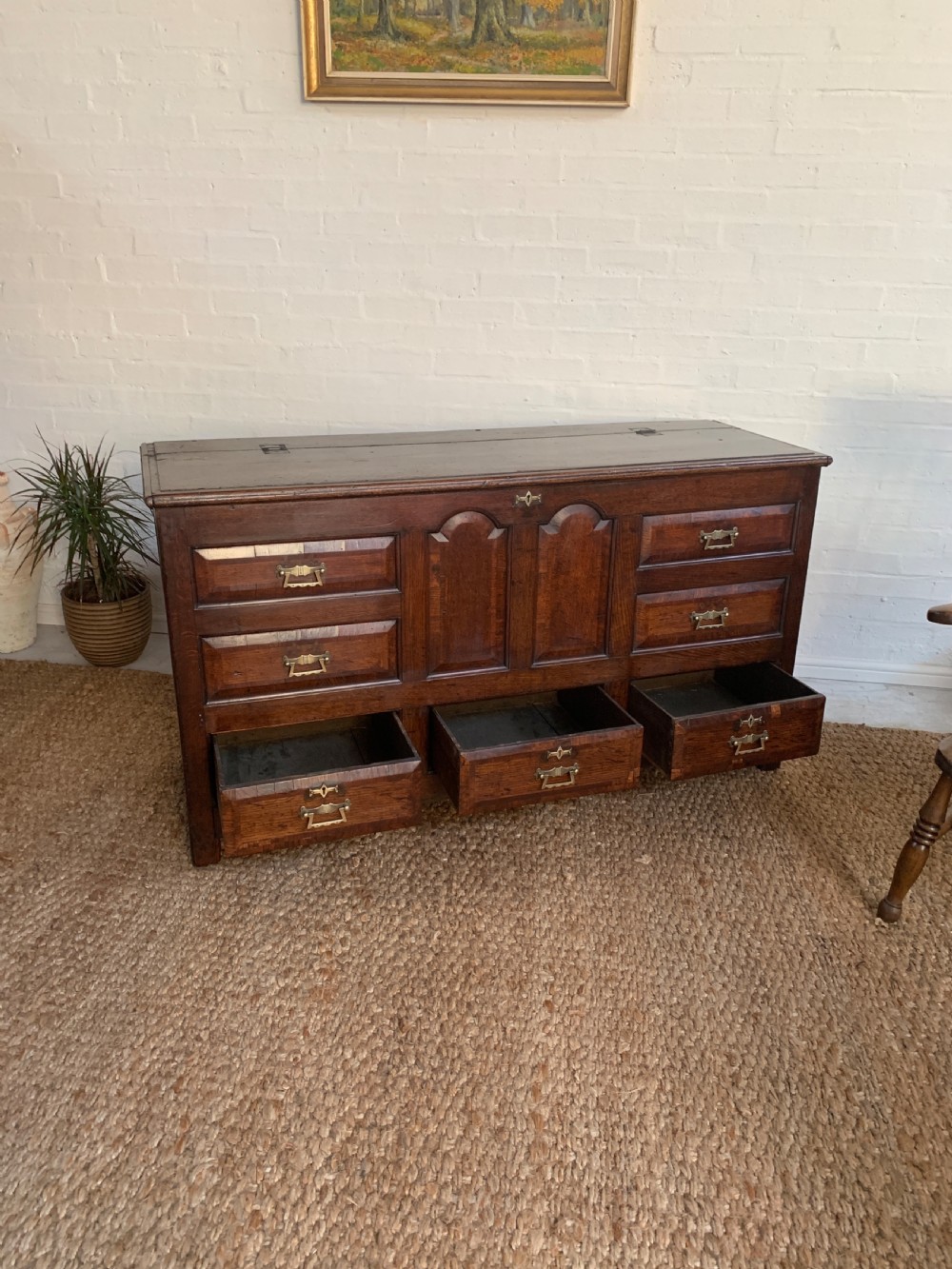 A dark oak mule chest featuring a hinged top, raised arched panels, multiple lower drawers, and brass batwing handles. View XI