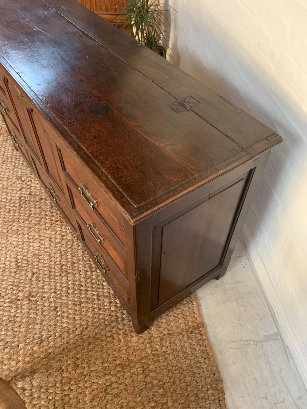 A dark oak mule chest featuring a hinged top, raised arched panels, multiple lower drawers, and brass batwing handles. View XIV