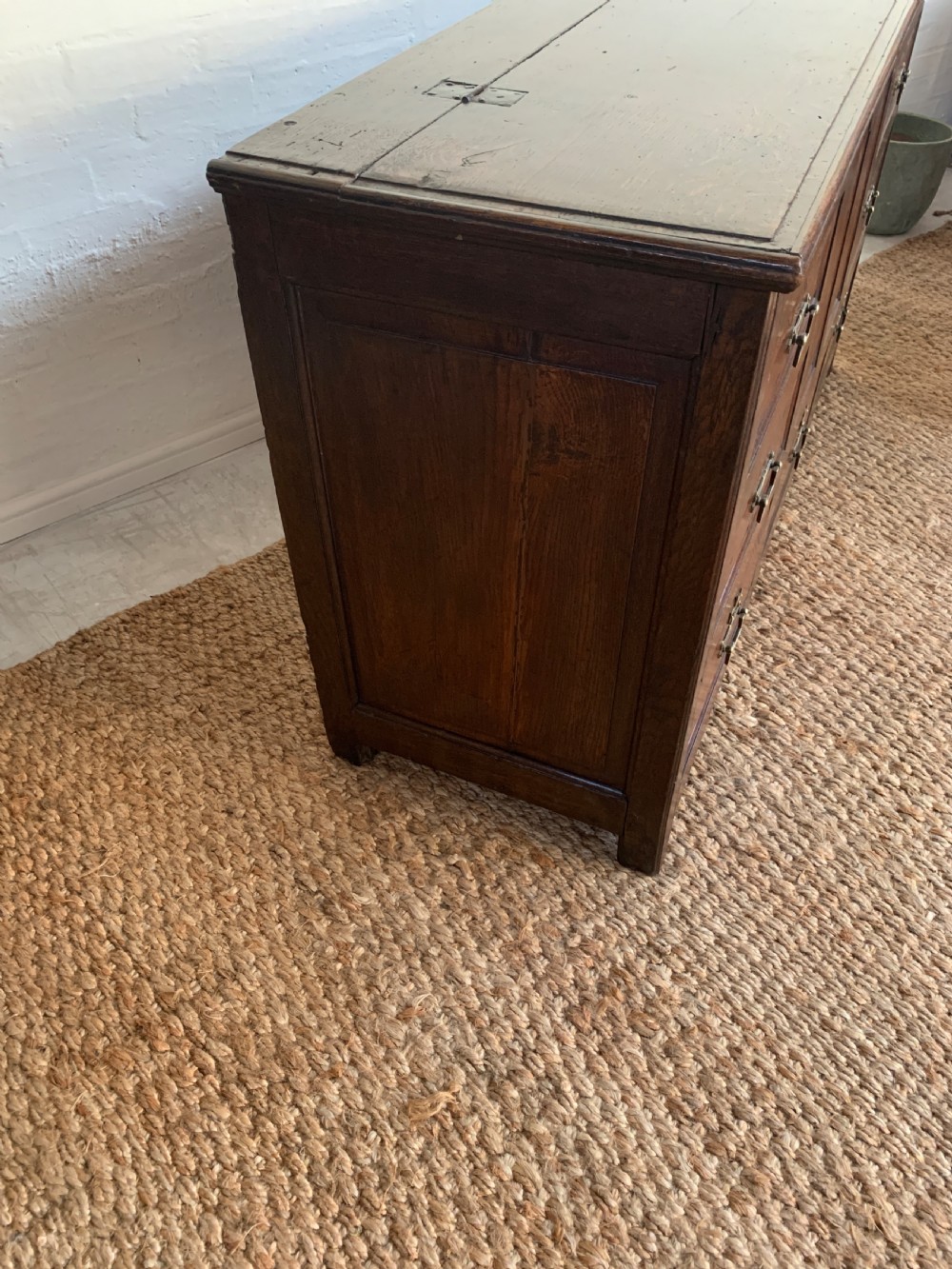 A dark oak mule chest featuring a hinged top, raised arched panels, multiple lower drawers, and brass batwing handles. View XV