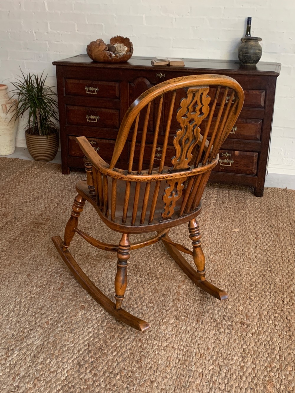 A nineteenth-century country-style Windsor rocking chair featuring a hoop back, central pierced splat, turned spindles, and shaped armrests on curved wooden rockers. View II