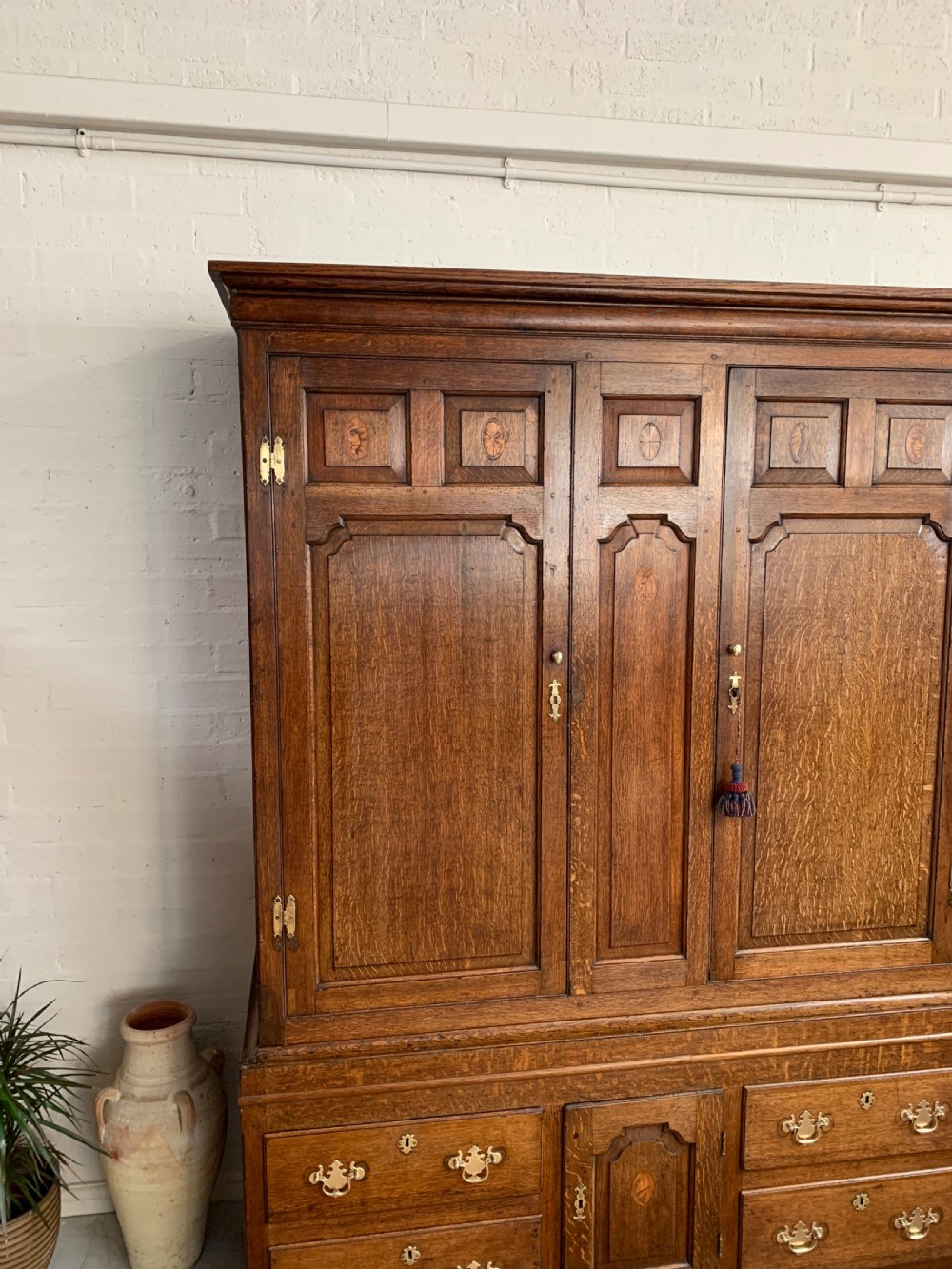 A late Georgian oak press cupboard featuring fielded panel doors with inlay motifs, H-hinges, and a base fitted with drawers and brass hardware. View II