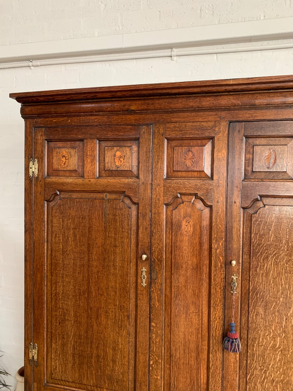 A late Georgian oak press cupboard featuring fielded panel doors with inlay motifs, H-hinges, and a base fitted with drawers and brass hardware. View III
