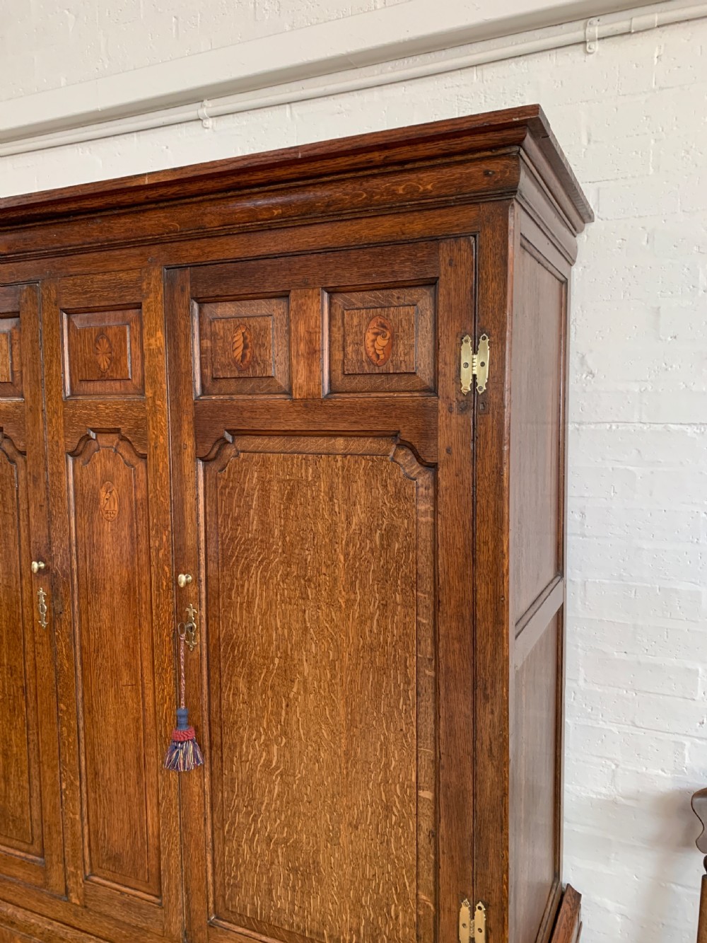 A late Georgian oak press cupboard featuring fielded panel doors with inlay motifs, H-hinges, and a base fitted with drawers and brass hardware. View V