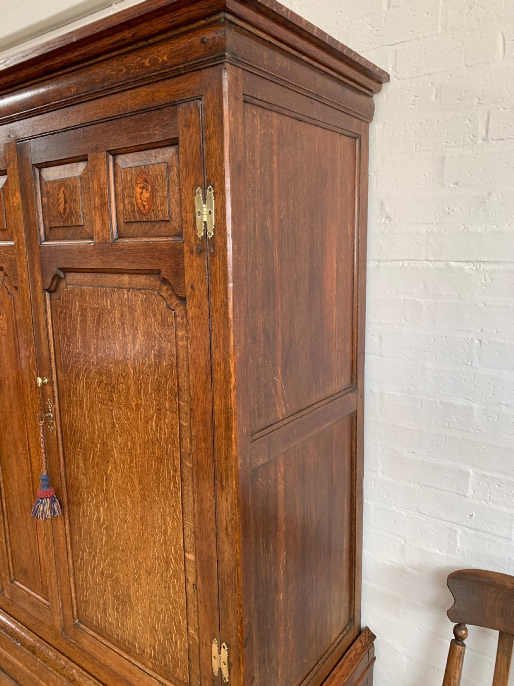 A late Georgian oak press cupboard featuring fielded panel doors with inlay motifs, H-hinges, and a base fitted with drawers and brass hardware. View VI