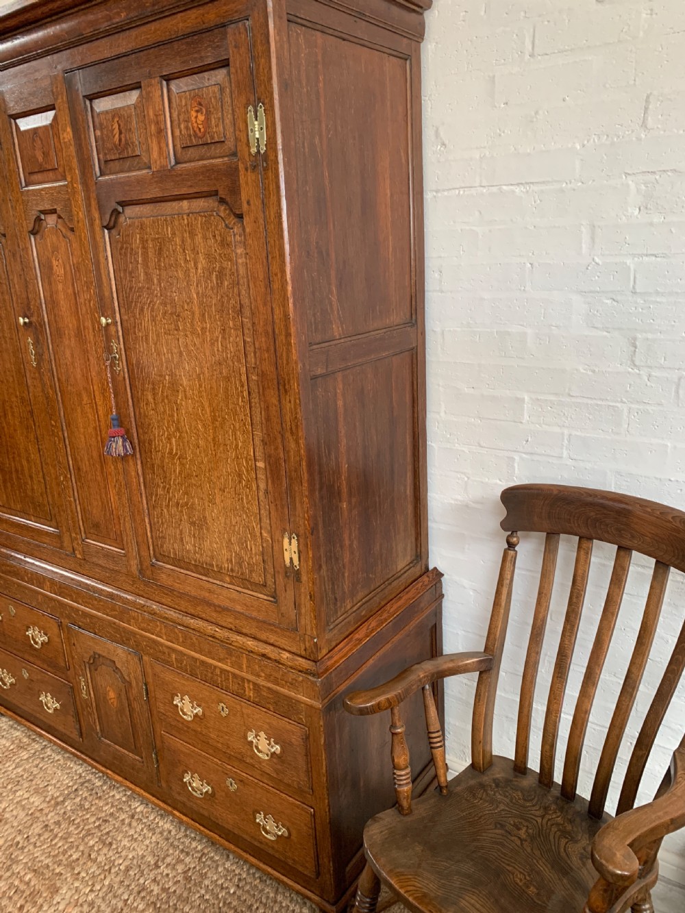 A late Georgian oak press cupboard featuring fielded panel doors with inlay motifs, H-hinges, and a base fitted with drawers and brass hardware. View VII