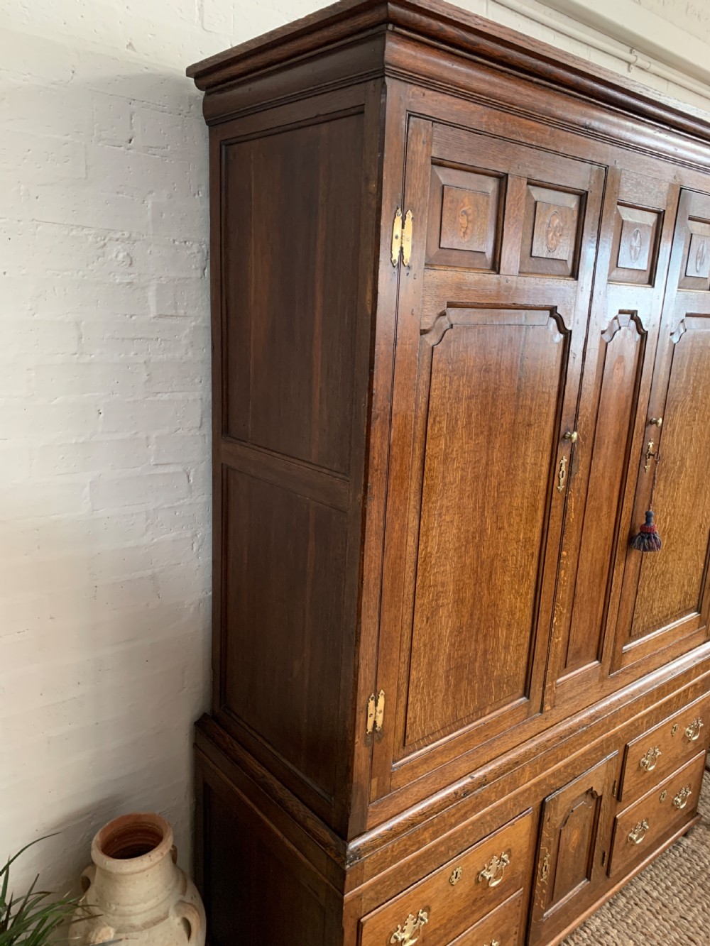 A late Georgian oak press cupboard featuring fielded panel doors with inlay motifs, H-hinges, and a base fitted with drawers and brass hardware. View VIII