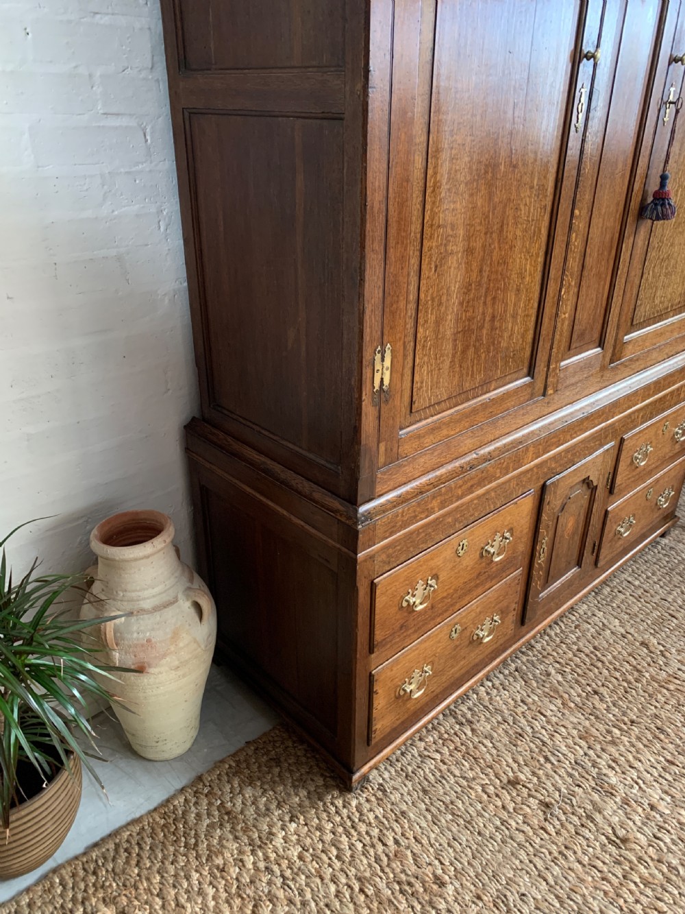 A late Georgian oak press cupboard featuring fielded panel doors with inlay motifs, H-hinges, and a base fitted with drawers and brass hardware. View IX