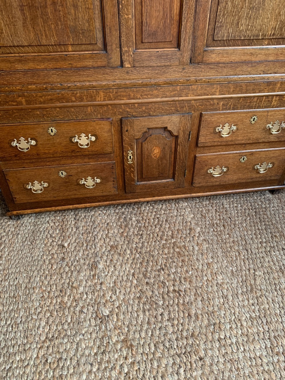 A late Georgian oak press cupboard featuring fielded panel doors with inlay motifs, H-hinges, and a base fitted with drawers and brass hardware. View X