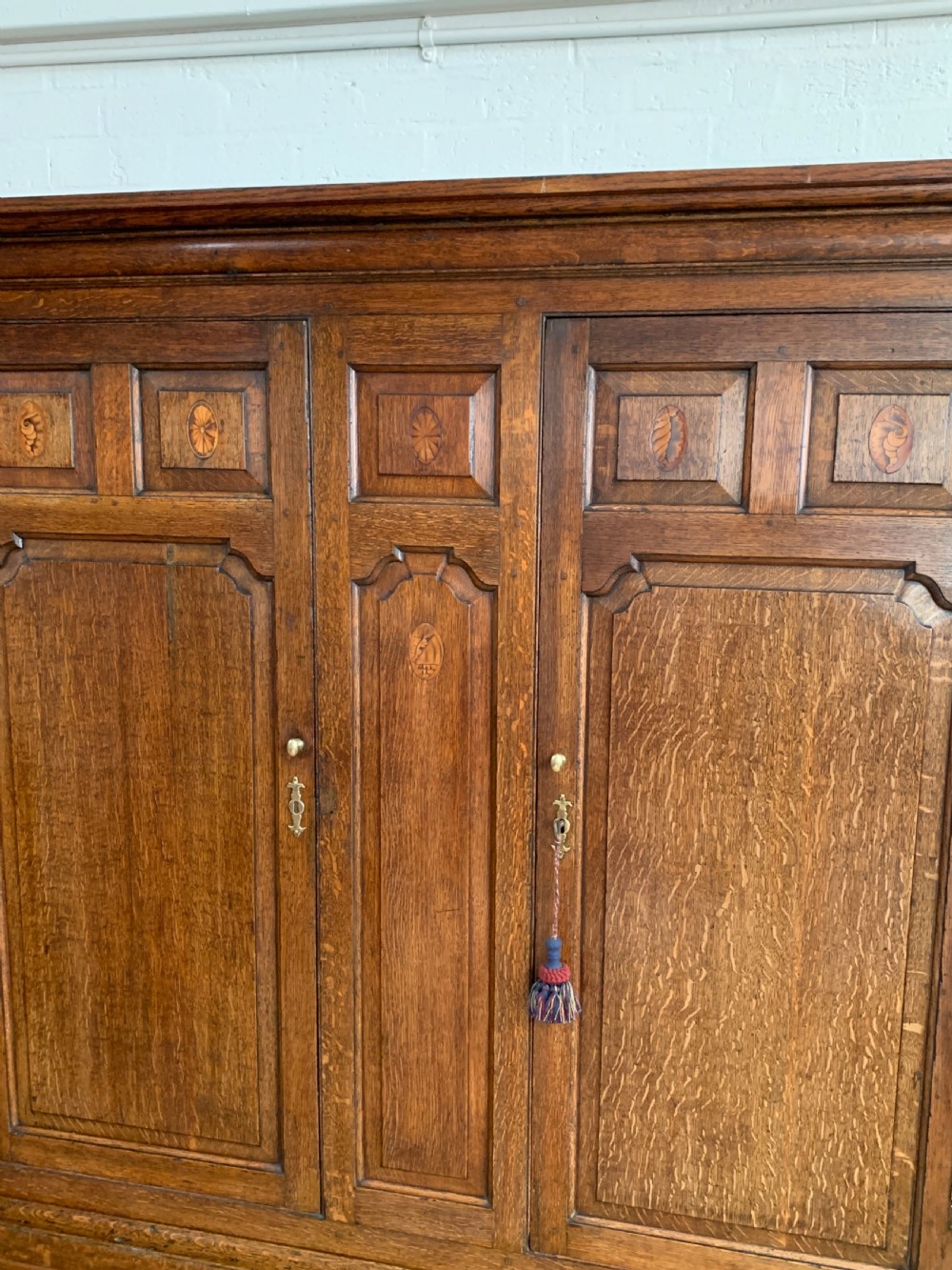 A late Georgian oak press cupboard featuring fielded panel doors with inlay motifs, H-hinges, and a base fitted with drawers and brass hardware. View XI