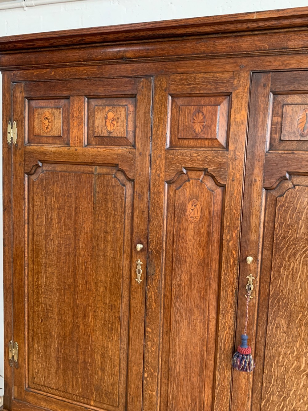 A late Georgian oak press cupboard featuring fielded panel doors with inlay motifs, H-hinges, and a base fitted with drawers and brass hardware. View XII